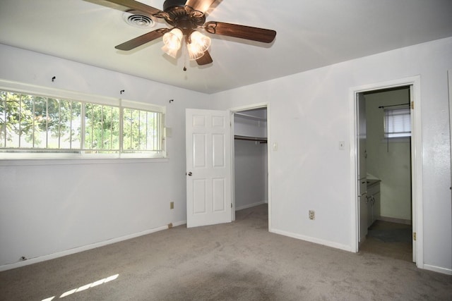 unfurnished bedroom featuring light colored carpet, ceiling fan, a spacious closet, connected bathroom, and a closet