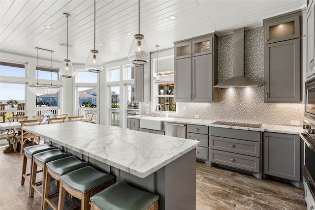 kitchen featuring appliances with stainless steel finishes, a kitchen island, hanging light fixtures, wall chimney exhaust hood, and dark wood-type flooring