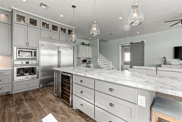 kitchen featuring dark wood-type flooring, built in appliances, hanging light fixtures, a barn door, and beverage cooler