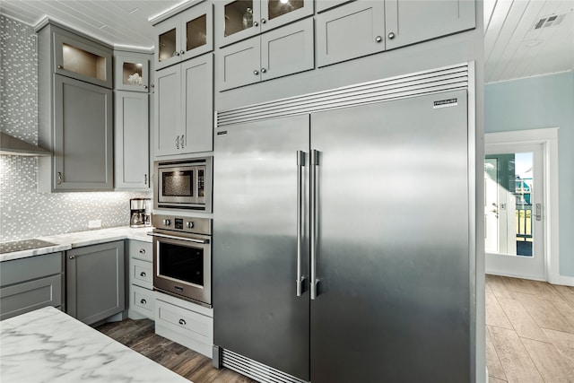 kitchen featuring built in appliances, light stone counters, gray cabinetry, and dark hardwood / wood-style flooring