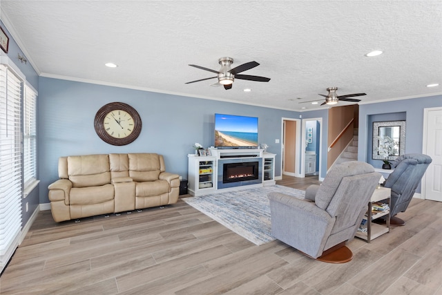 living room featuring ceiling fan, ornamental molding, a textured ceiling, and light wood-type flooring