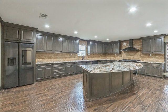 kitchen with sink, a kitchen island, wall chimney range hood, stainless steel appliances, and dark hardwood / wood-style flooring