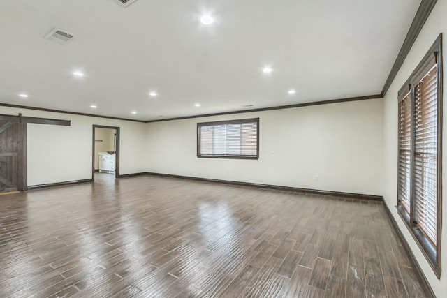 spare room with a barn door, dark hardwood / wood-style floors, and crown molding