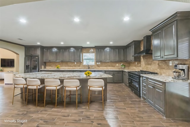 kitchen with black gas range oven, wall chimney range hood, stainless steel refrigerator with ice dispenser, and a kitchen island