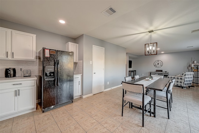 kitchen with light tile patterned floors, backsplash, an inviting chandelier, white cabinetry, and black fridge