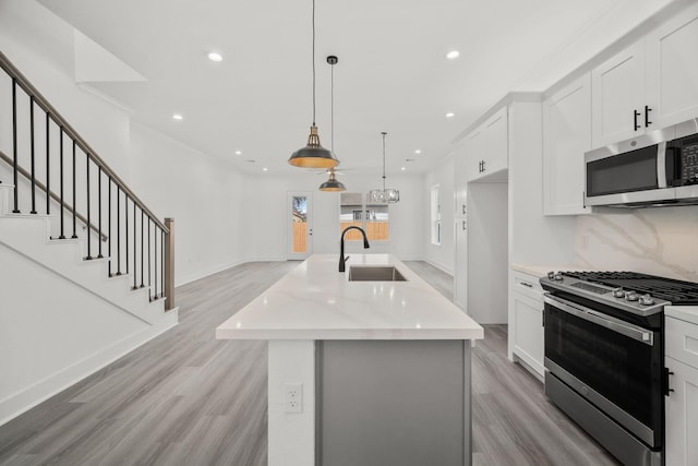 kitchen with decorative light fixtures, a center island with sink, sink, stainless steel appliances, and white cabinets