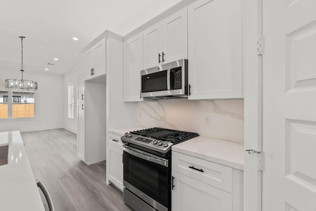 kitchen featuring stainless steel appliances, backsplash, hanging light fixtures, white cabinets, and light stone counters