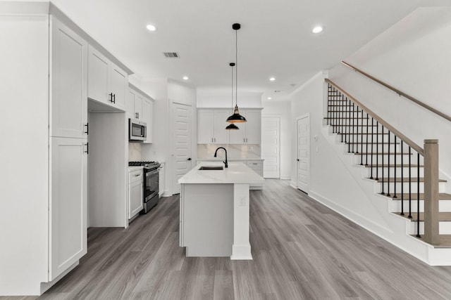 kitchen featuring white cabinets, appliances with stainless steel finishes, hanging light fixtures, a kitchen island with sink, and light wood-type flooring