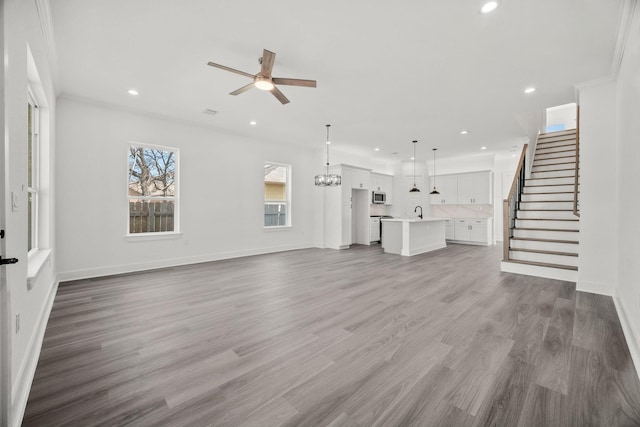 unfurnished living room featuring crown molding, ceiling fan with notable chandelier, wood-type flooring, and sink