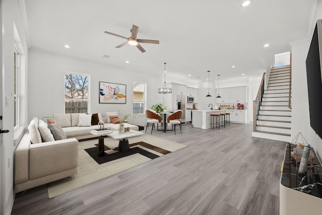 living room featuring ceiling fan with notable chandelier, ornamental molding, light hardwood / wood-style floors, and sink