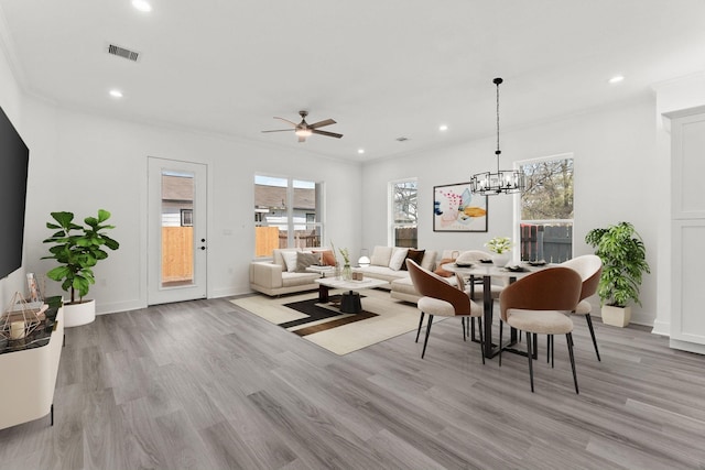 living room featuring a wealth of natural light, ceiling fan with notable chandelier, ornamental molding, and light hardwood / wood-style flooring