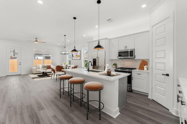 kitchen featuring white cabinets, an island with sink, stainless steel appliances, and pendant lighting