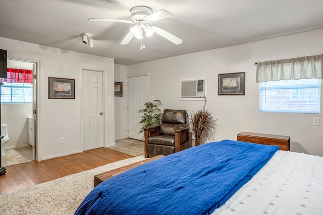 bedroom featuring a wall mounted air conditioner, ensuite bath, ceiling fan, multiple windows, and light hardwood / wood-style floors