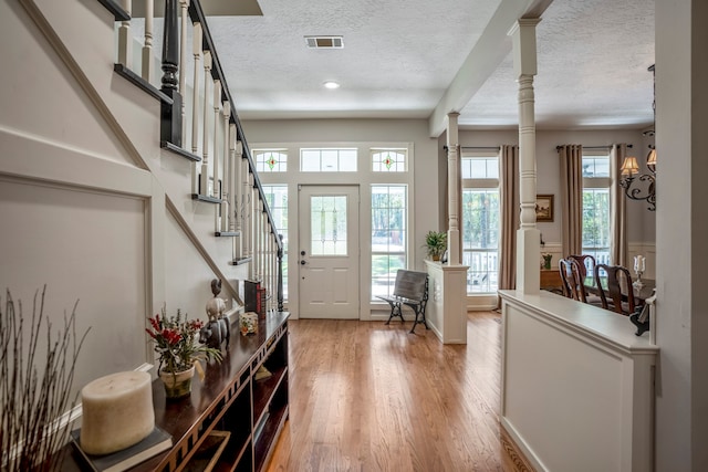 entryway featuring ornate columns, a chandelier, a textured ceiling, and hardwood / wood-style flooring