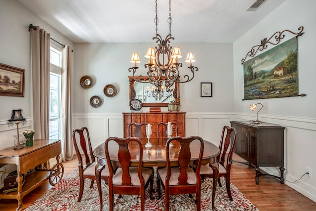 dining space with light wood-type flooring, a textured ceiling, and an inviting chandelier