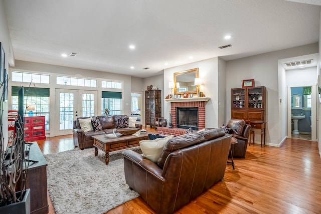 living room featuring french doors, light wood-type flooring, a brick fireplace, and sink