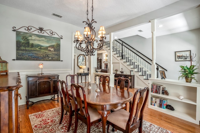 dining space with built in shelves, decorative columns, a chandelier, wood-type flooring, and a textured ceiling