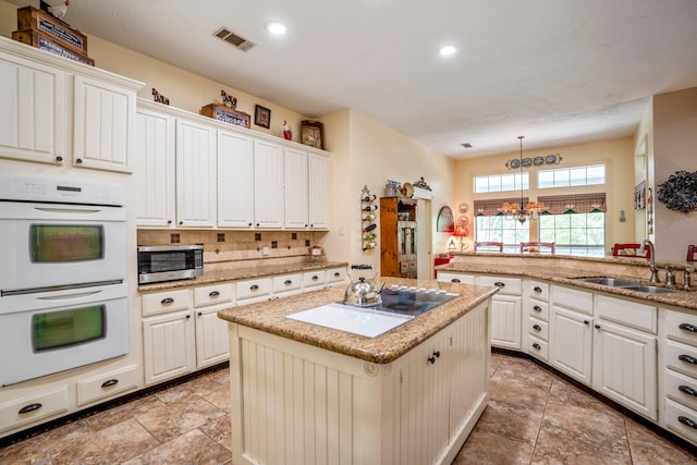 kitchen featuring sink, a center island, double oven, a chandelier, and electric stovetop