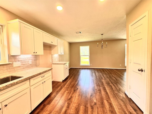 kitchen featuring light stone countertops, white cabinetry, dark wood-type flooring, tasteful backsplash, and a notable chandelier