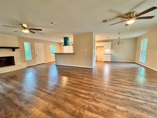 unfurnished living room featuring a fireplace, ceiling fan with notable chandelier, and dark wood-type flooring