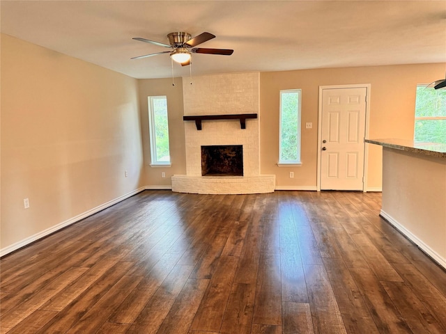 unfurnished living room featuring a wealth of natural light, dark hardwood / wood-style flooring, ceiling fan, and a brick fireplace