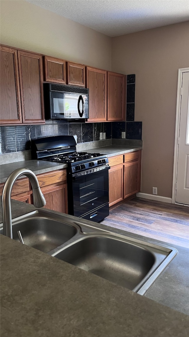 kitchen featuring hardwood / wood-style flooring, a textured ceiling, tasteful backsplash, and black appliances