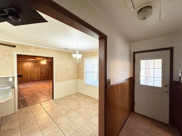 entryway featuring light tile patterned flooring, crown molding, plenty of natural light, and an inviting chandelier