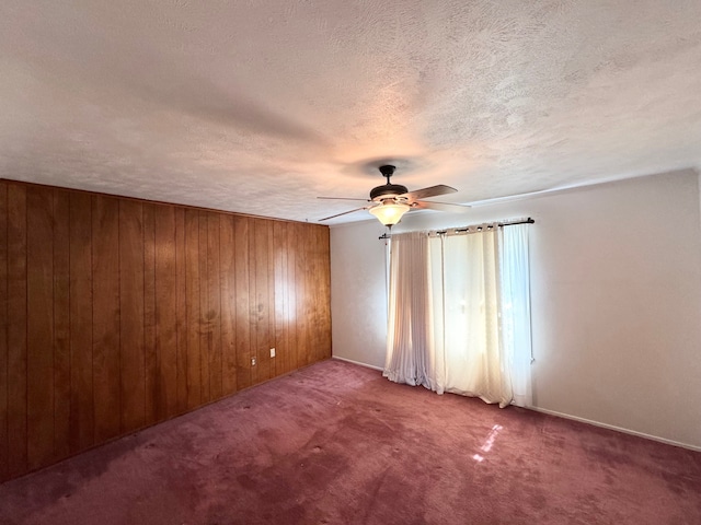 unfurnished room featuring ceiling fan, a textured ceiling, wood walls, and carpet