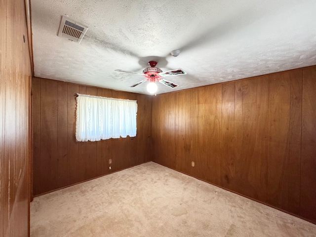 spare room with carpet floors, wood walls, ceiling fan, and a textured ceiling