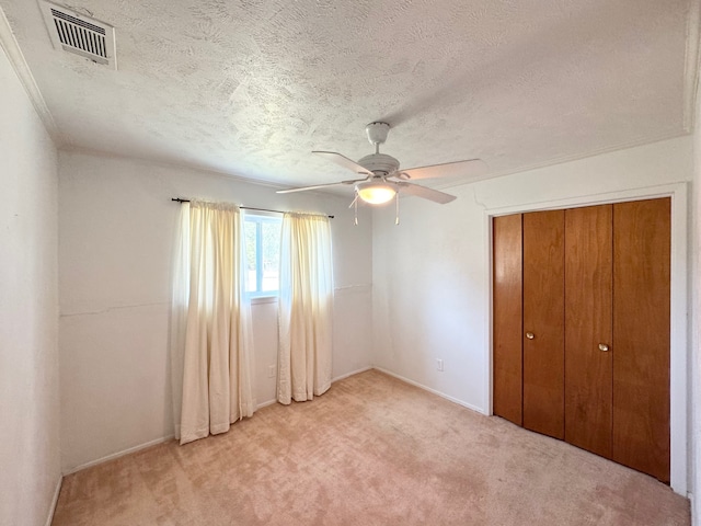 unfurnished bedroom with light carpet, ceiling fan, a closet, and a textured ceiling