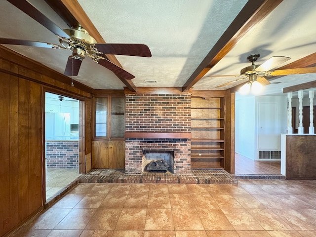 unfurnished living room with beam ceiling, wood walls, and a textured ceiling