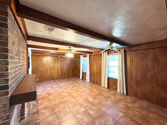 unfurnished living room featuring ceiling fan, a textured ceiling, wooden walls, and beam ceiling