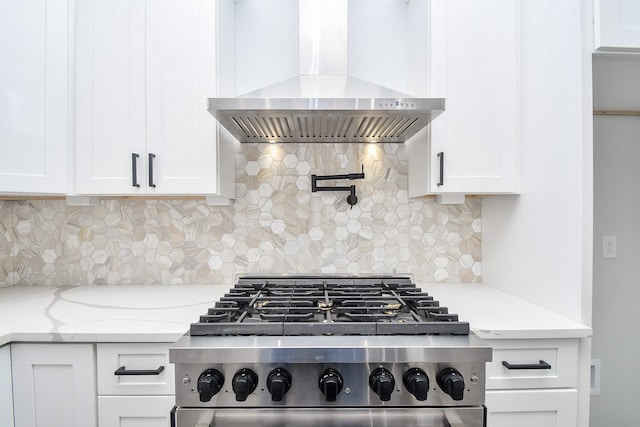 kitchen featuring wall chimney exhaust hood, white cabinetry, light stone counters, and stainless steel stove