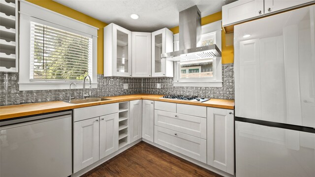 kitchen featuring wood counters, stainless steel appliances, wall chimney exhaust hood, and white cabinets