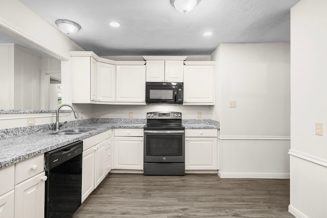 kitchen with sink, light stone countertops, dark hardwood / wood-style floors, white cabinets, and black appliances