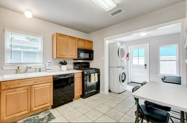 kitchen featuring light tile patterned floors, sink, stacked washing maching and dryer, and black appliances