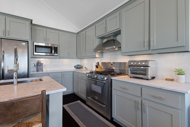 kitchen featuring lofted ceiling, gray cabinetry, appliances with stainless steel finishes, range hood, and backsplash