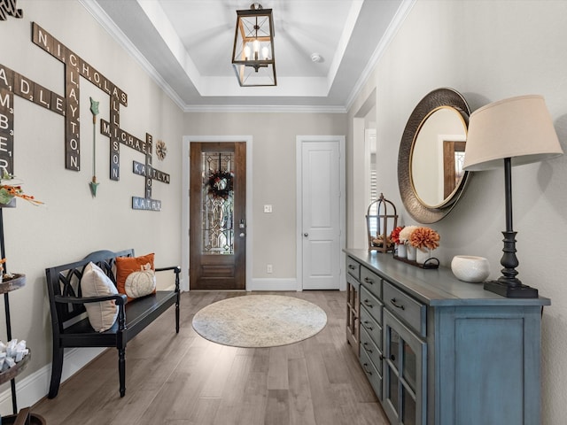 foyer with light wood-type flooring, a tray ceiling, and ornamental molding