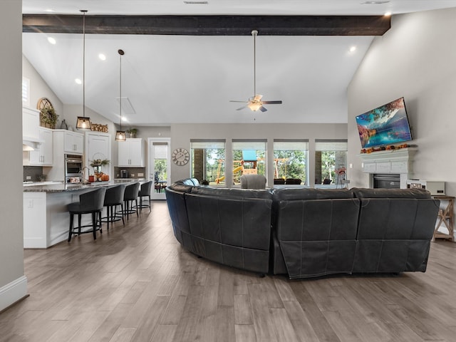 living room featuring beamed ceiling, ceiling fan, a healthy amount of sunlight, and light wood-type flooring