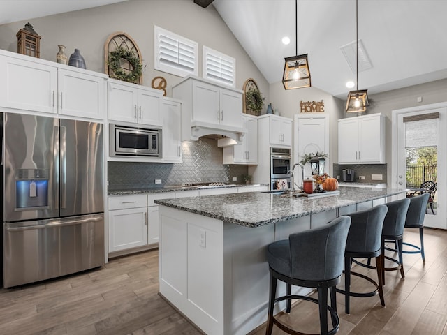 kitchen featuring backsplash, a kitchen island with sink, white cabinets, lofted ceiling with beams, and appliances with stainless steel finishes