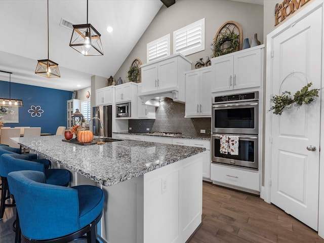 kitchen with tasteful backsplash, a center island with sink, stainless steel appliances, and decorative light fixtures