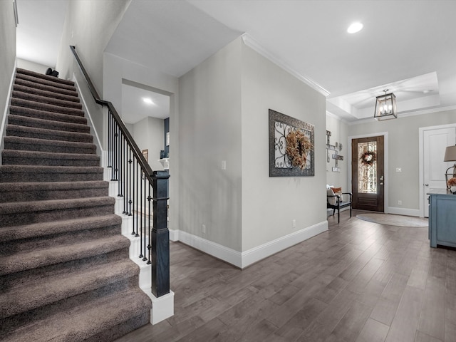 entryway with a notable chandelier, a raised ceiling, wood-type flooring, and crown molding