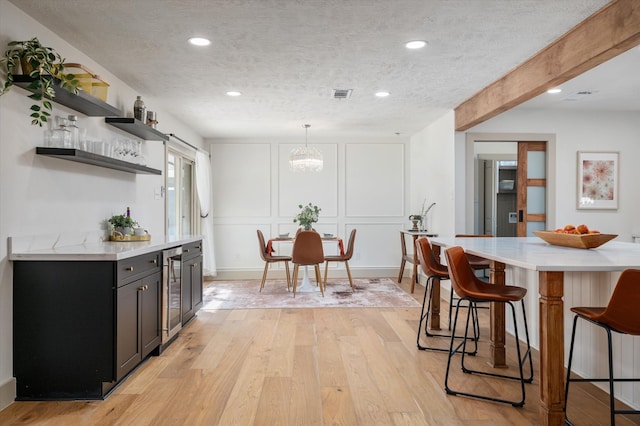 kitchen featuring pendant lighting, a breakfast bar, a textured ceiling, light hardwood / wood-style floors, and beverage cooler