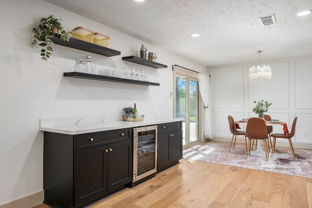 bar featuring wine cooler, pendant lighting, light hardwood / wood-style floors, and a textured ceiling