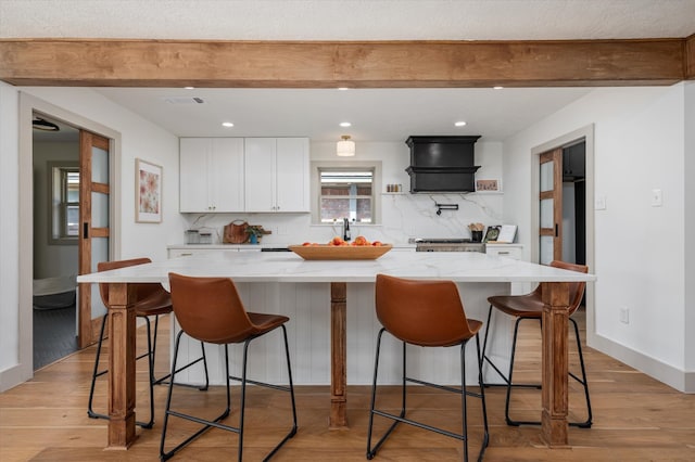 kitchen with a kitchen bar, light stone countertops, light wood-type flooring, white cabinets, and a kitchen island