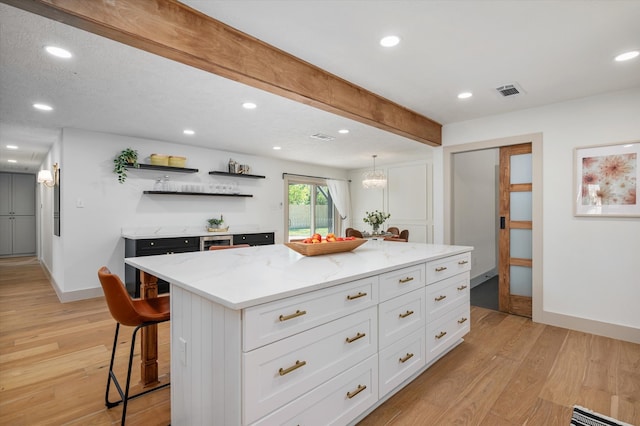 kitchen featuring light stone countertops, a center island, light hardwood / wood-style floors, and white cabinetry