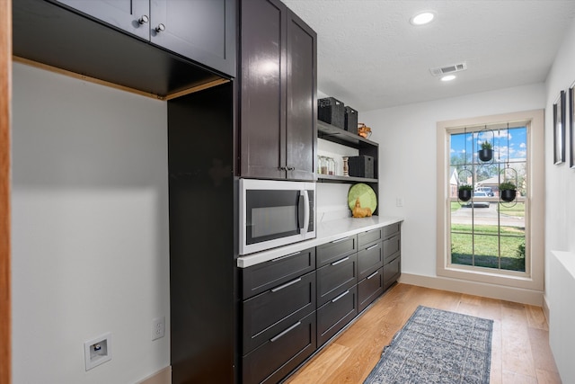 kitchen with stainless steel microwave, a textured ceiling, and light hardwood / wood-style flooring