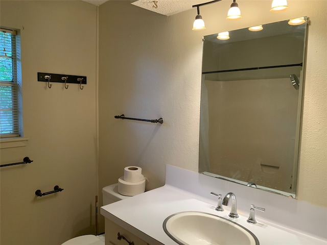 bathroom featuring a textured ceiling, walk in shower, vanity, and toilet