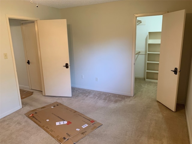 unfurnished bedroom featuring a textured ceiling, light colored carpet, and a walk in closet