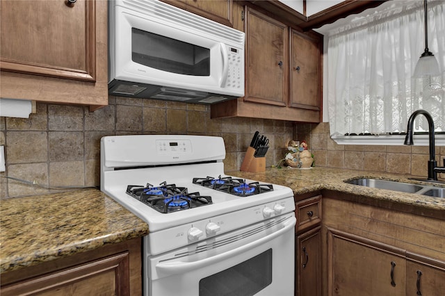 kitchen with pendant lighting, sink, white appliances, tasteful backsplash, and light stone countertops